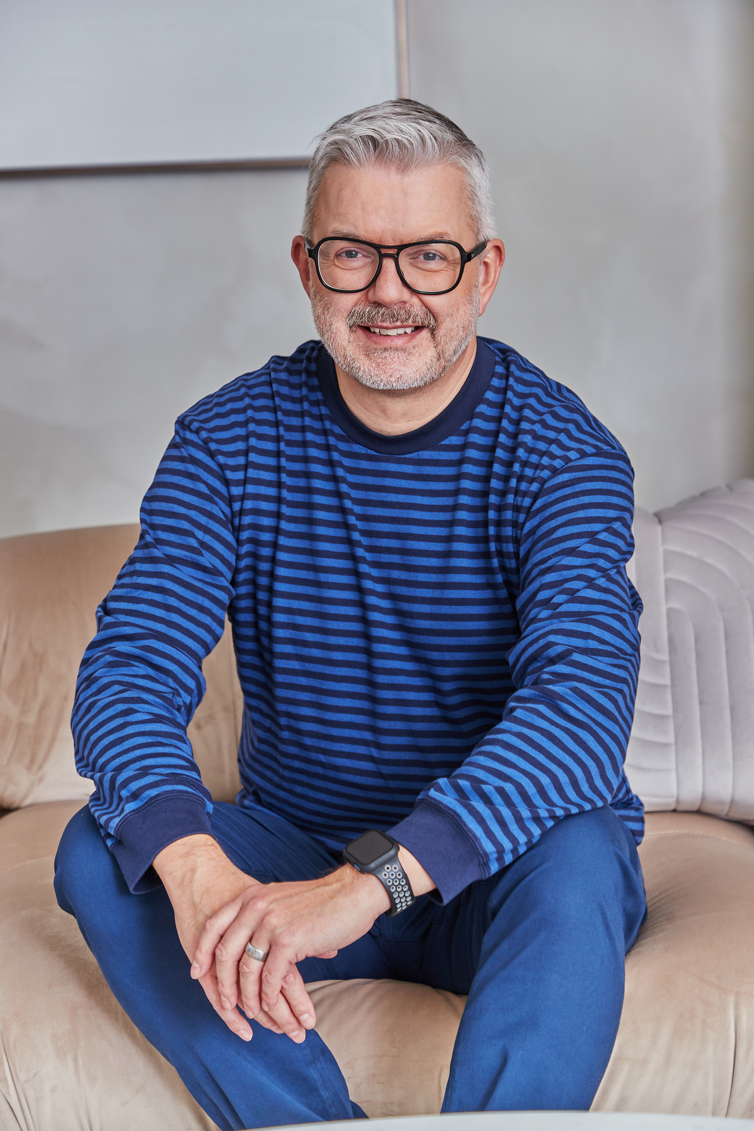 Smiling man in a blue striped sweater seated on a sofa, lifestyle portrait