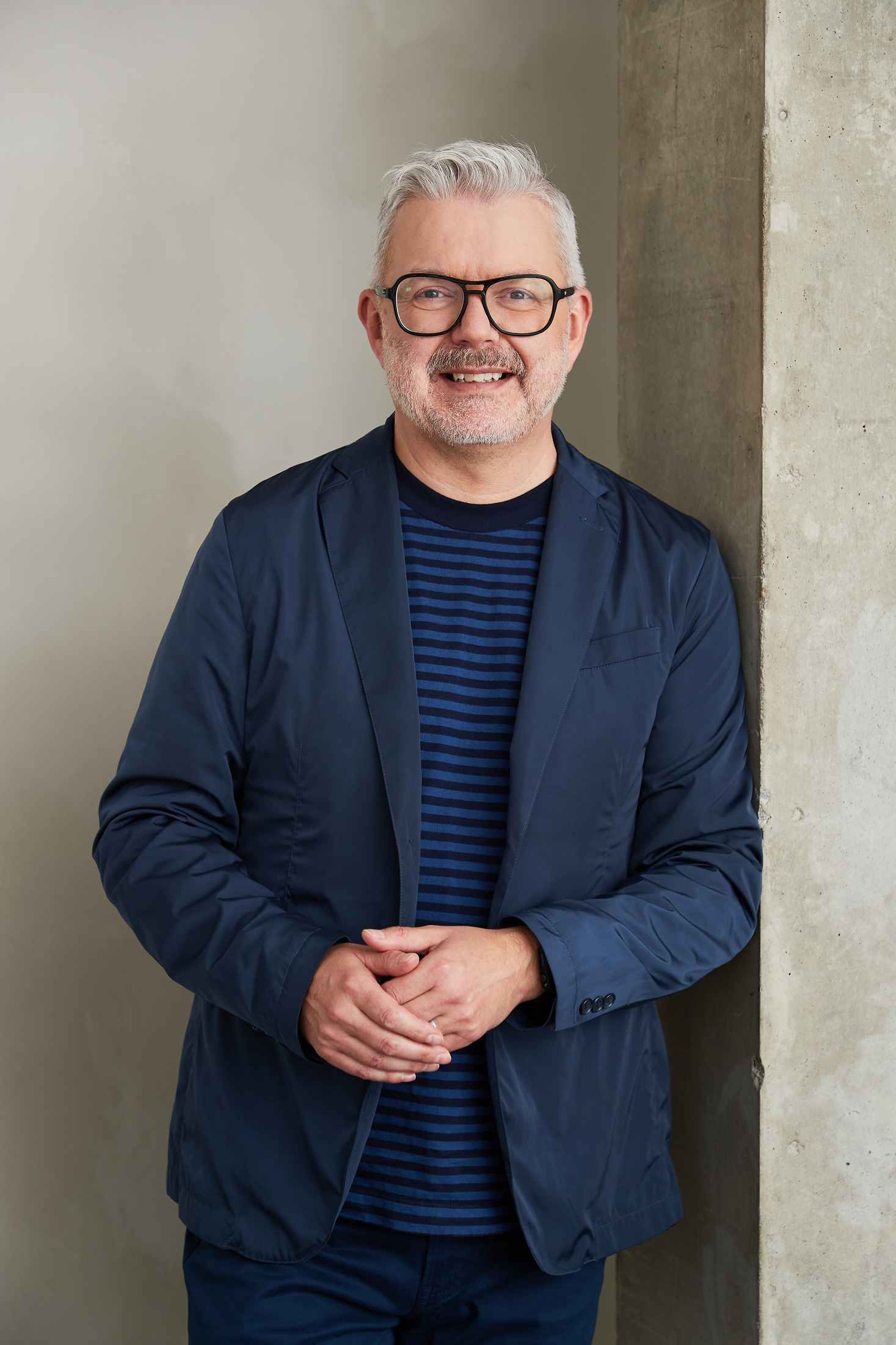Man in a navy blazer leaning against a concrete wall, professional portrait
