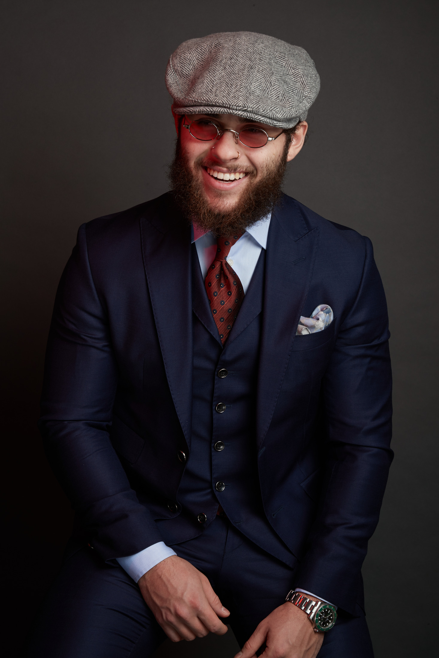 Portrait of a bearded man in a three-piece navy suit and flat cap