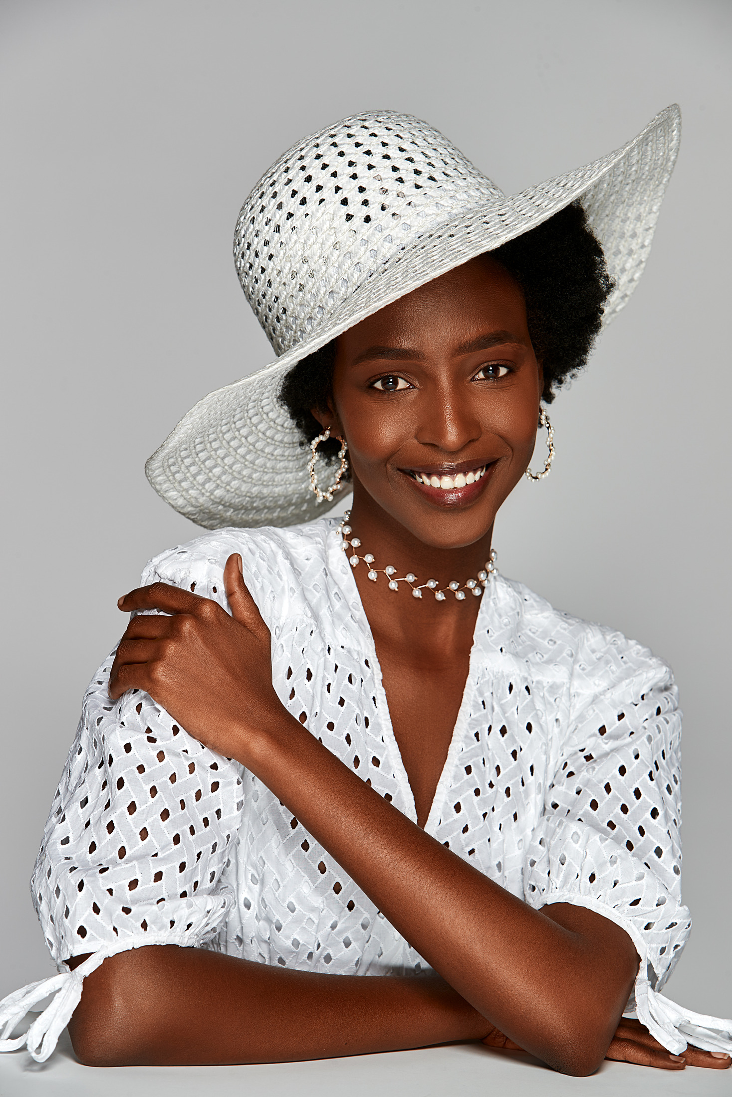 Portrait of a smiling woman in a white sun hat and eyelet blouse on a grey backdrop