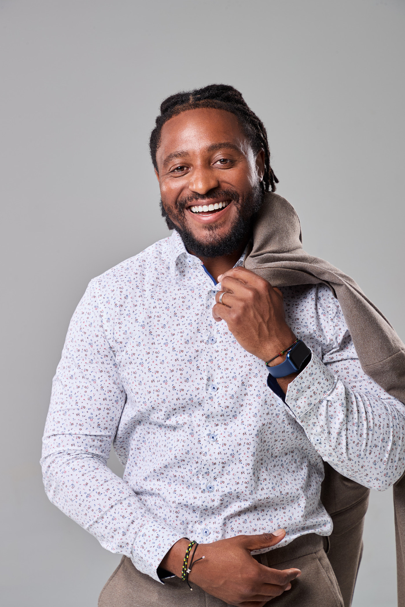 Man in a patterned shirt smiling with a jacket over his shoulder, grey studio portrait