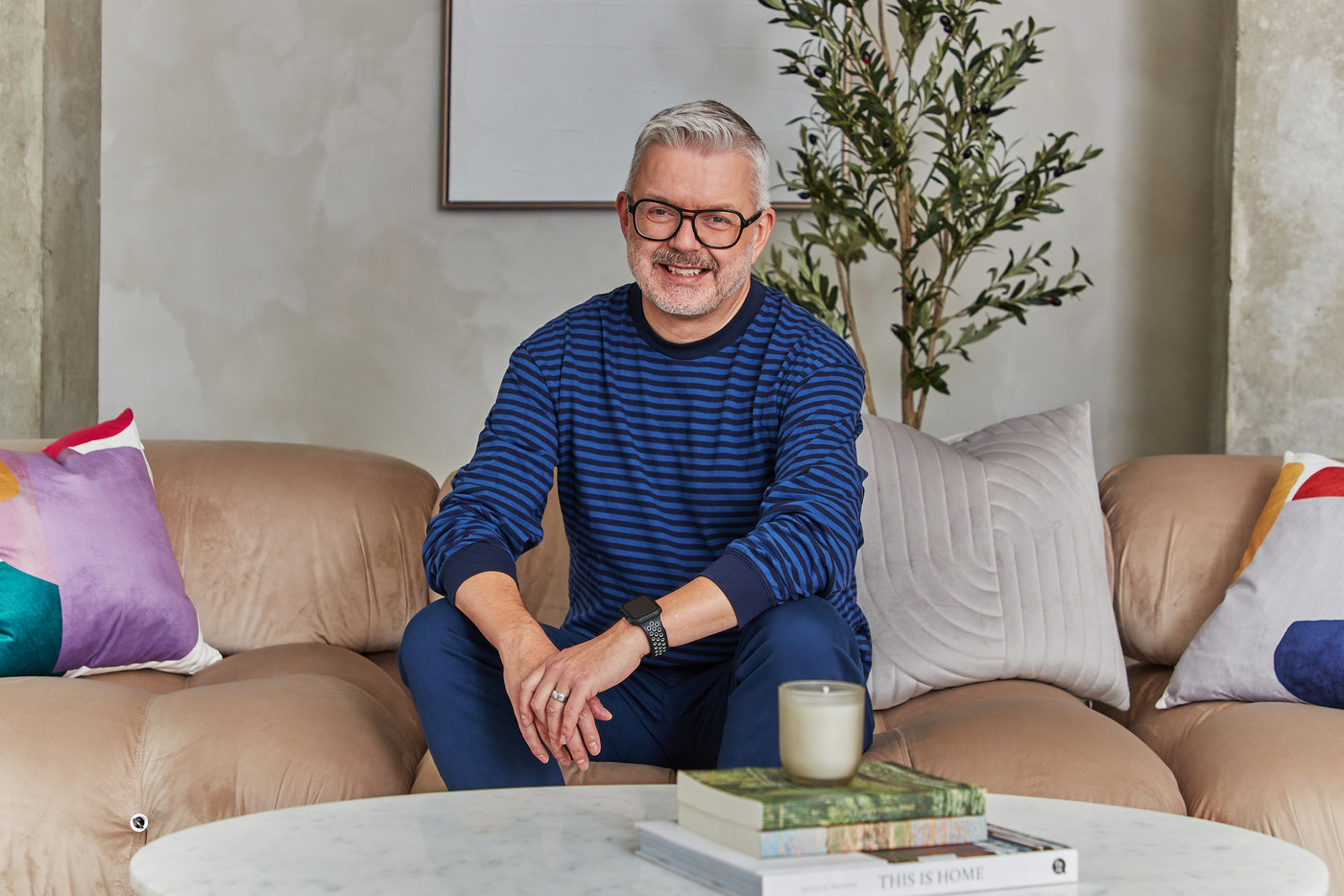 Smiling man in a striped sweater on a beige modular sofa, lifestyle portrait